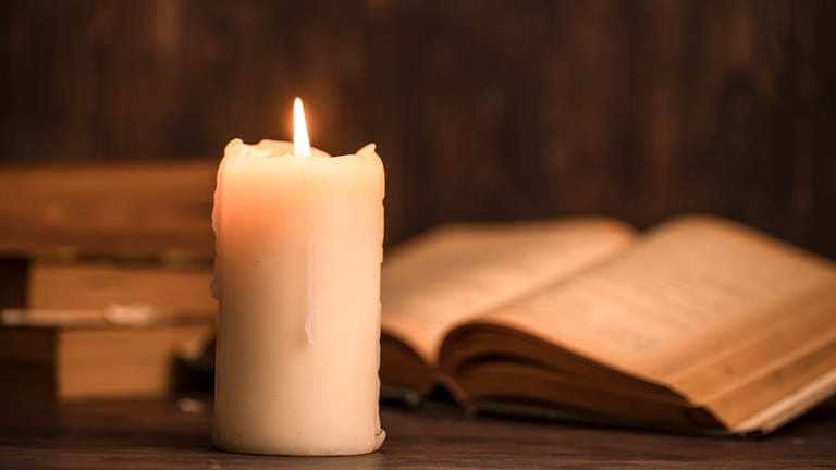 Eine brennende Kerze steht vor einem aufgeklappten Buch