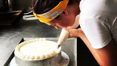 Eine junge Frau arbeitet in einer Konditorei an einer Torte. 