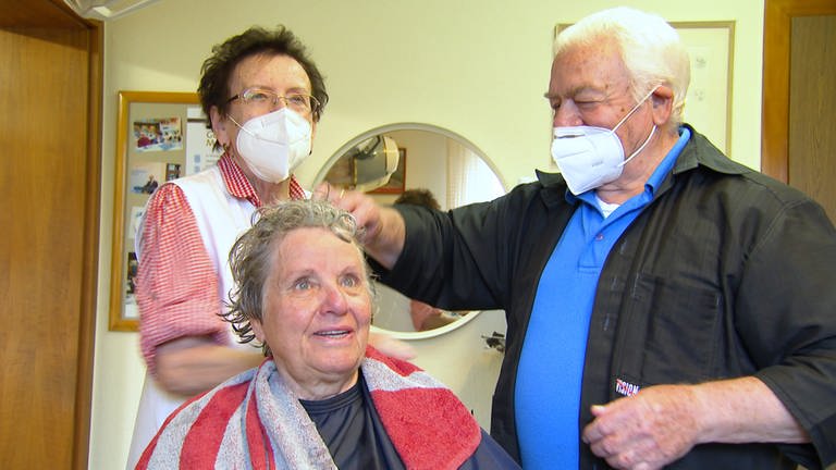 Ein altes Ehepaar schneidet einer Kundin in ihrem Salon die Haare