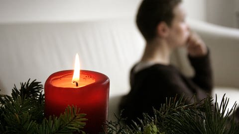 Trauer und Einsamkeit an Weihnachten: Eine nachdenkliche Frau bei Kerzenlicht.