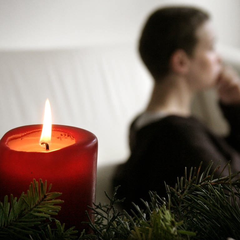 Trauer und Einsamkeit an Weihnachten: Eine nachdenkliche Frau bei Kerzenlicht.
