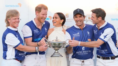 Prinz Harry im Trikot samt seinem Polo-Team und in der Mitte mit Meghan in einem weißen Kleid halten gemeinsam die Trophäe nach einem gewonnen Spiel in Florida.
