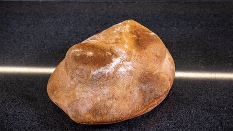 Der Brotlaib mit Braten im Inneren liegt fertig gebacken auf der Arbeitsfläche: Der Kassler im Brotteig ist laut Rezept fertig, wenn er goldgelb gebacken ist.