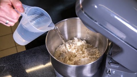 Wasser wird in eine Rührschüssel mit Mehl und Hefe geschüttet: Der Hefeteig für den Kassler im Brotteig muss laut Rezept gründlich verrührt werden.