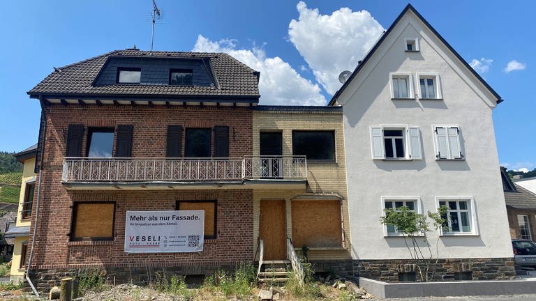 Von der Flutkatastrophe im Ahrtal betroffene Häuser in Dernau - zwei noch mit Brettern vernagelt, ein drittes bereits neu verputzt.