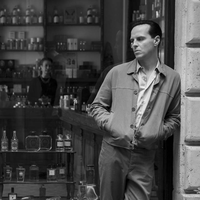 Andrew Scott als Tom Ripley. Er lehnt im Rahmen des Schaufensters einer Bar.